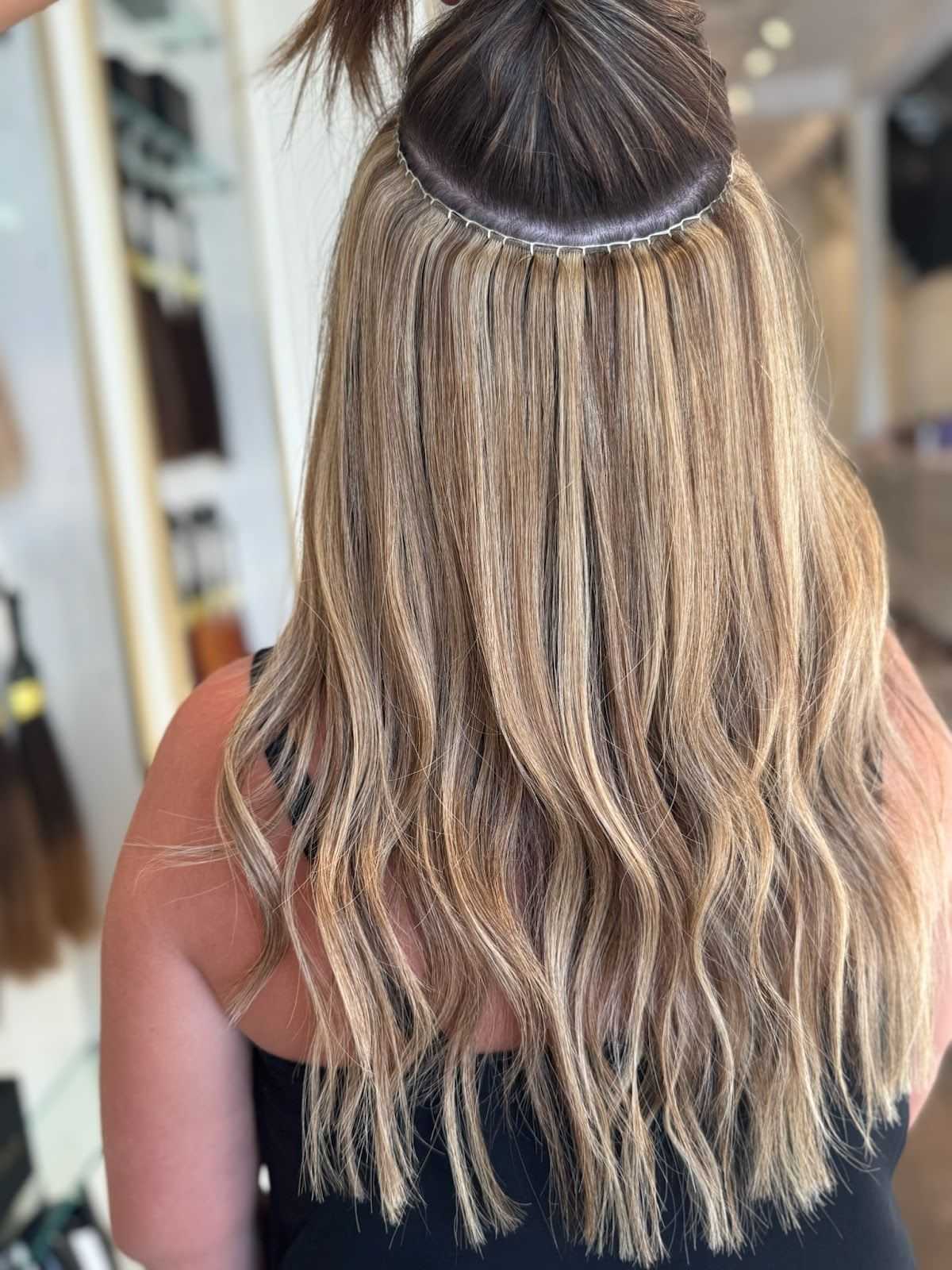 Blonde hair with extensions applied, viewed from the back in a salon setting.