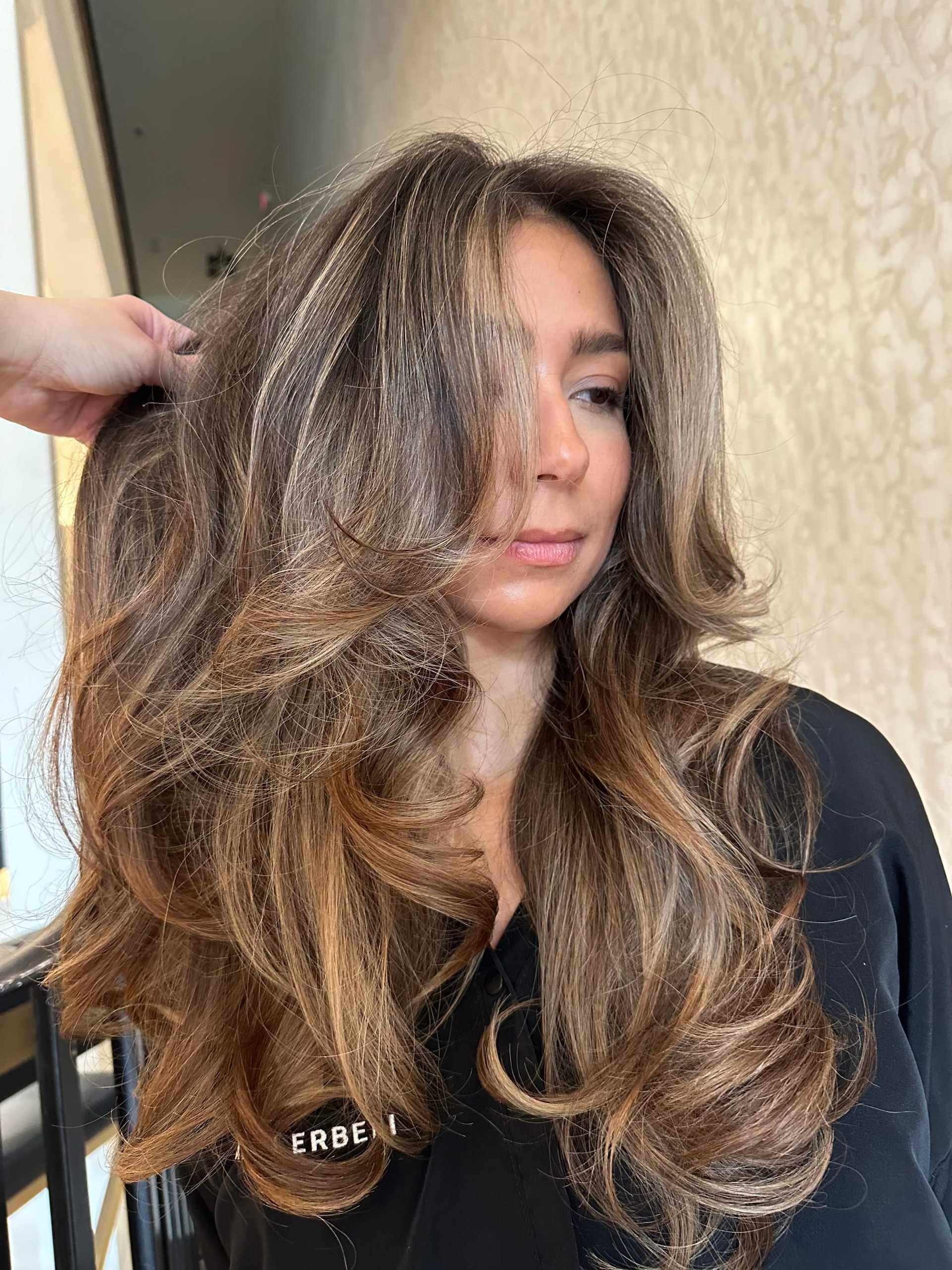 Long, voluminous wavy hairstyle showcased by a woman in a salon setting.