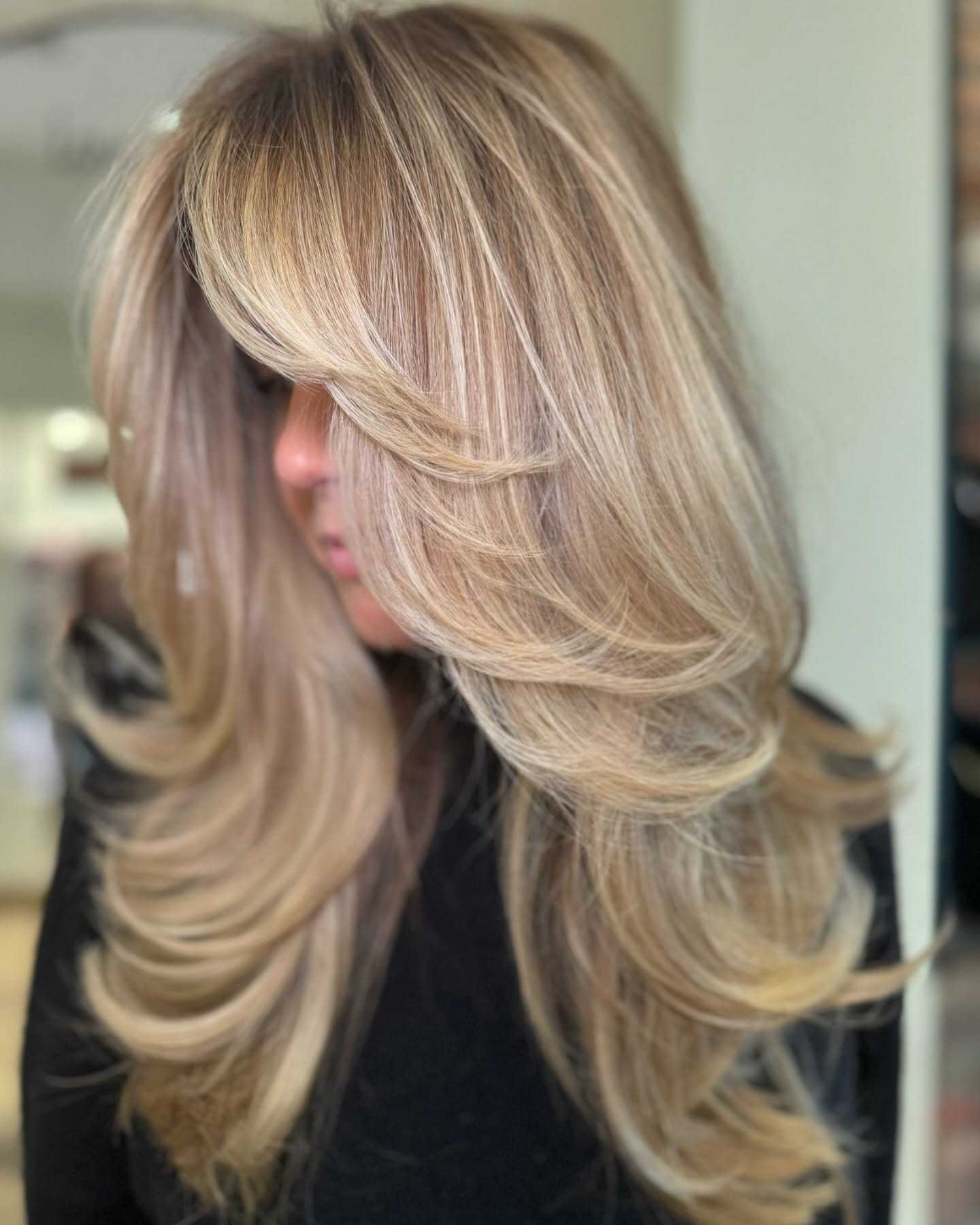 Long, layered blonde hairstyle with voluminous waves and face-framing bangs.