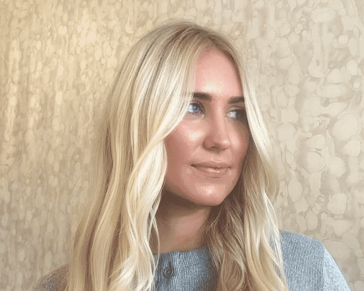 Blonde woman with long hair in a gray shirt, textured wall background.